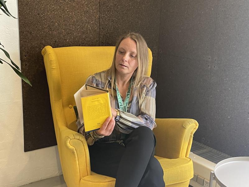 Nina sidder i en gul stol og læser i en bog.