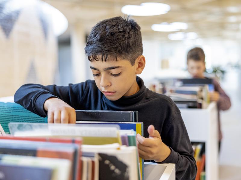 Dreng står og bladrer i bøger