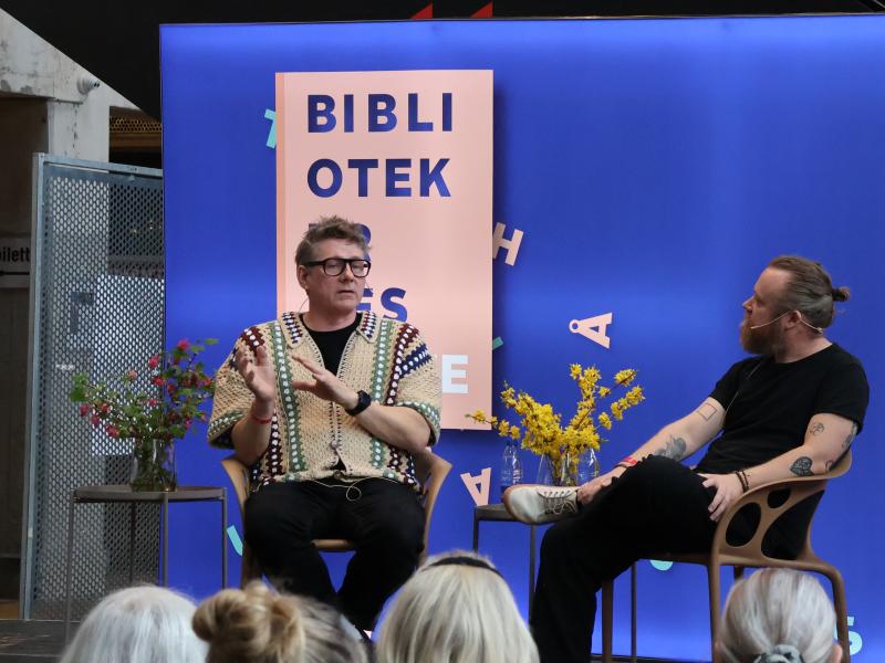 To mennesker, Jørgen (tv) og Teis (tv) sidder på en scene og taler foran et publikum