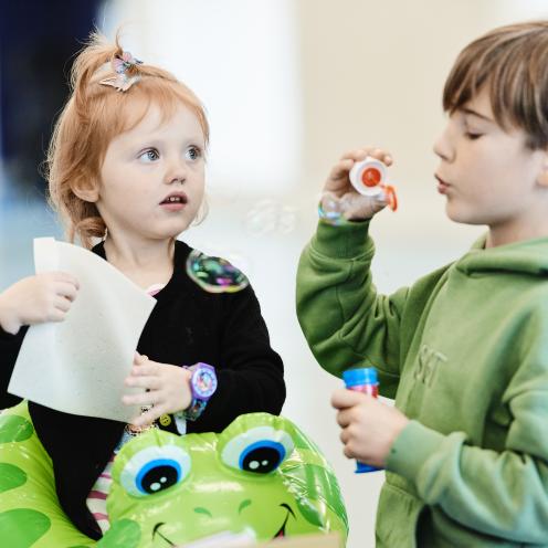 En dreng puster sæbebobler, mens en pige kigger på ham.