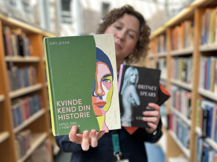 Ditte står blandt bogreoler og holder de tre omtalte bøger i denne artikel i hænderne. Hun holder "Kvinde kend din historie" frem for sig, så der er mest fokus på denne bogforside. Baggrunden er let sløret.